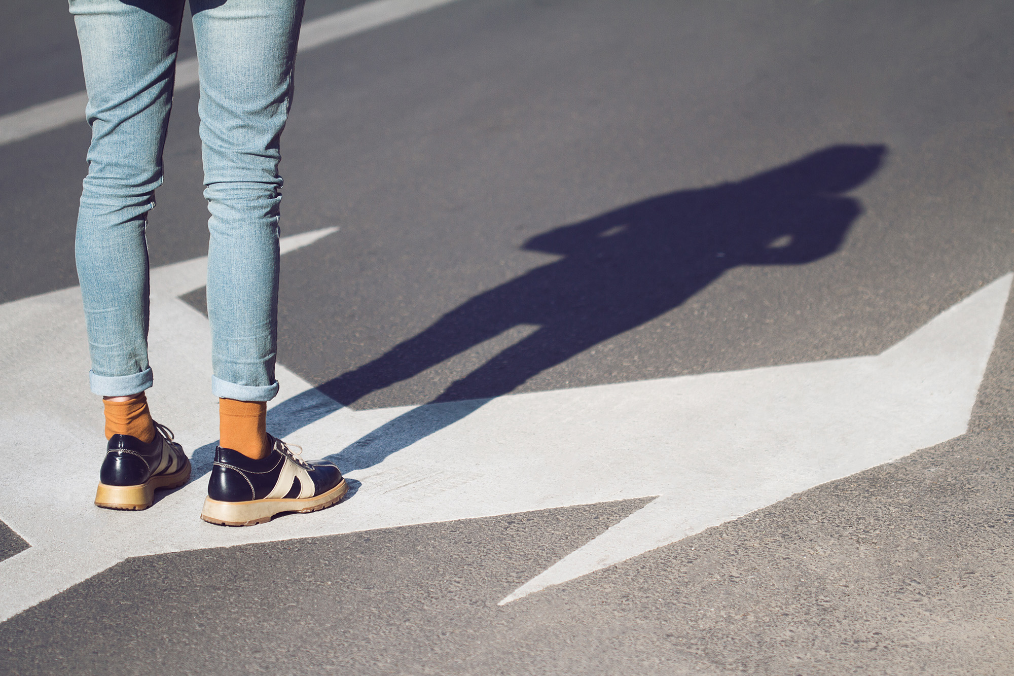 Symbolbild Orientierung(slosigkeit). Nahaufnahme von Frau Schuhe stehen auf der Straße. In zwei Richtungen abbiegender Pfeil auf Strasse.